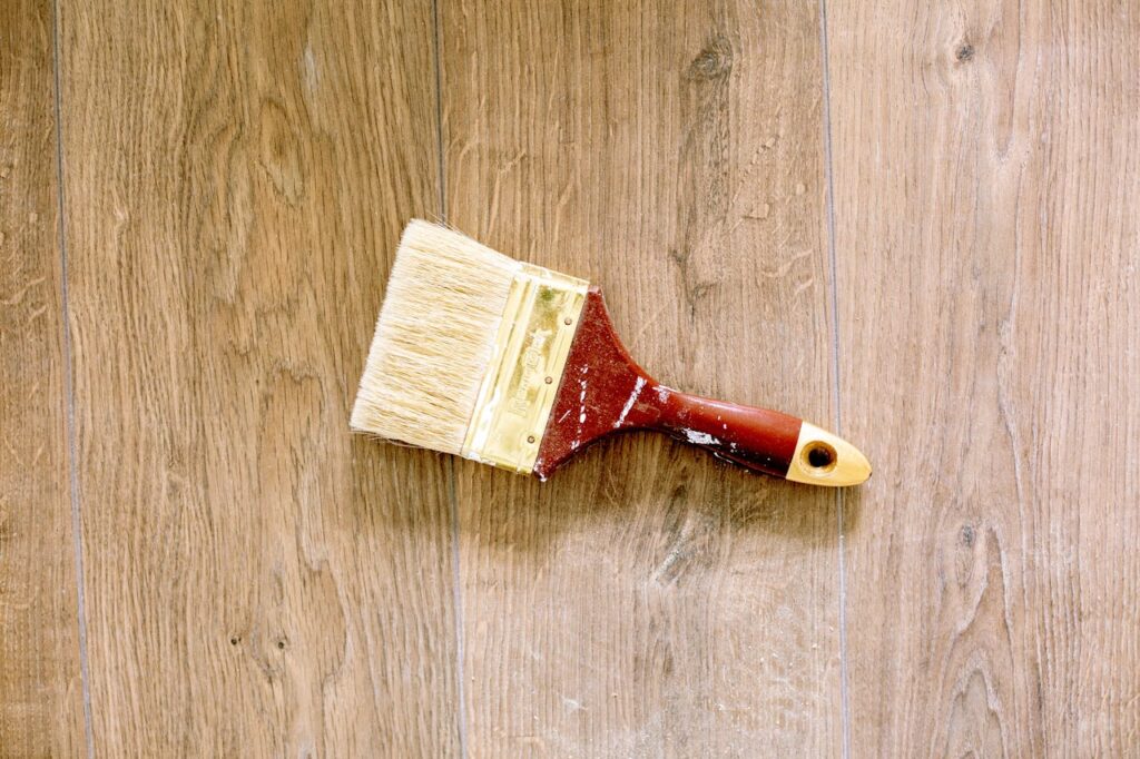 A used paintbrush lying on a wooden floor, ideal for renovation and DIY themes.
